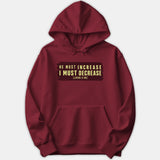 A maroon hoodie featuring a graphic block print that reads 'He Must Increase I Must Decrease' with the scripture reference John 3:30 in light yellow text.