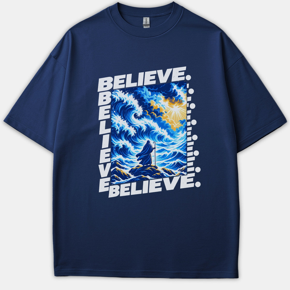 A navy blue t-shirt featuring a dramatic graphic of a robed figure before parting ocean waves under divine sunlight, framed by the word BELIEVE in bold white text.
