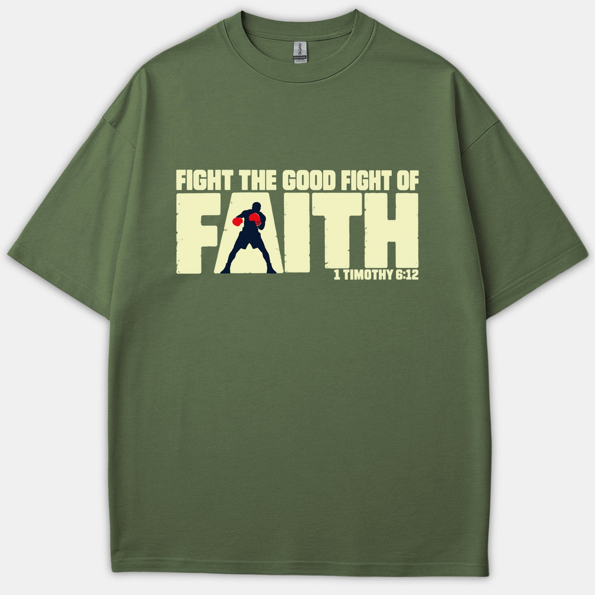 An olive green t-shirt featuring the graphic text 'FIGHT THE GOOD FIGHT OF FAITH' with a boxer silhouette cut out inside the word 'FAITH' and 1 Timothy 6:12 printed below.