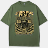 A green graphic t-shirt featuring a wooden cross with a receipt nailed to it, reading 'Jesus Paid It All' with Colossians 2:13-14.