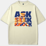 A beige t-shirt featuring bold navy and orange typography that reads 'ASK SEEK KNOCK MATT 7:7' with an image of a person praying silhouette within the lettering.