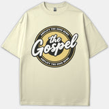A beige Christian t-shirt featuring a circular emblem graphic with the text 'the Gospel' in bold script and 'AMPLIFY THE GOOD NEWS' along the black and gold border.
