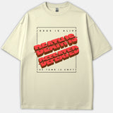 A beige T-shirt featuring a framed graphic with bold red 3D lettering reading 'DEATH IS DEFEATED' accompanied by the text 'JESUS IS ALIVE' and 'THE TOMB IS EMPTY'.
