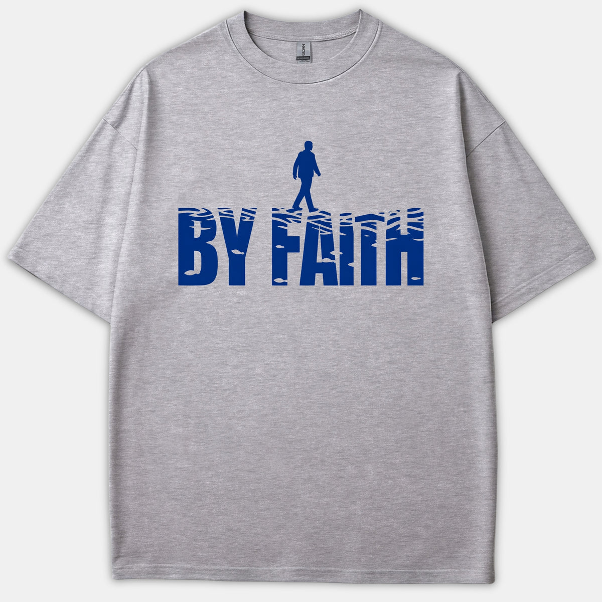 A gray Christian t-shirt featuring a blue graphic reading BY FAITH styled as water waves with a silhouette of a person walking on top.