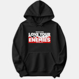 A black pullover hoodie featuring a bold Christian graphic print that reads 'Jesus Said Love Your Enemies' with scripture reference Matthew 5:44 in red and white.