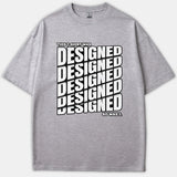 A heather gray t-shirt featuring bold black and white typography that reads 'THIS T-SHIRT WAS DESIGNED SO WAS I.' across the front.