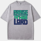 A heather gray Christian t-shirt featuring bold, block typography that reads PRAISE THE LORD in teal green and navy blue graphics across the front.