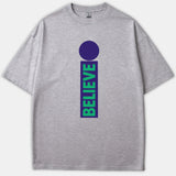 A heather gray t-shirt featuring a purple lowercase letter i graphic with the word BELIEVE written vertically in green inside the stem.