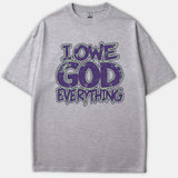 A gray t-shirt featuring the text 'I OWE GOD EVERYTHING' in a distressed purple font outlined in green.