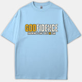 A light blue Christian t-shirt featuring a graphic that reads Godfidence Knowing I Can't But He Can in bold yellow and white text.