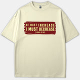 A beige Christian t-shirt featuring a red painted banner graphic printed with the scripture quote 'HE MUST INCREASE I MUST DECREASE [JOHN 3:30]' in yellow text.