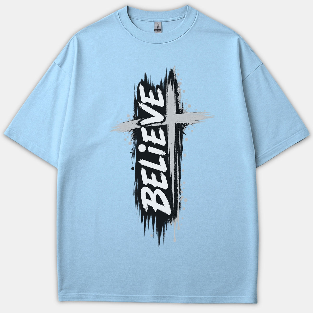 A light blue Christian t-shirt featuring a distressed black and gray cross graphic with the word BELIEVE printed vertically in bold white brush font.