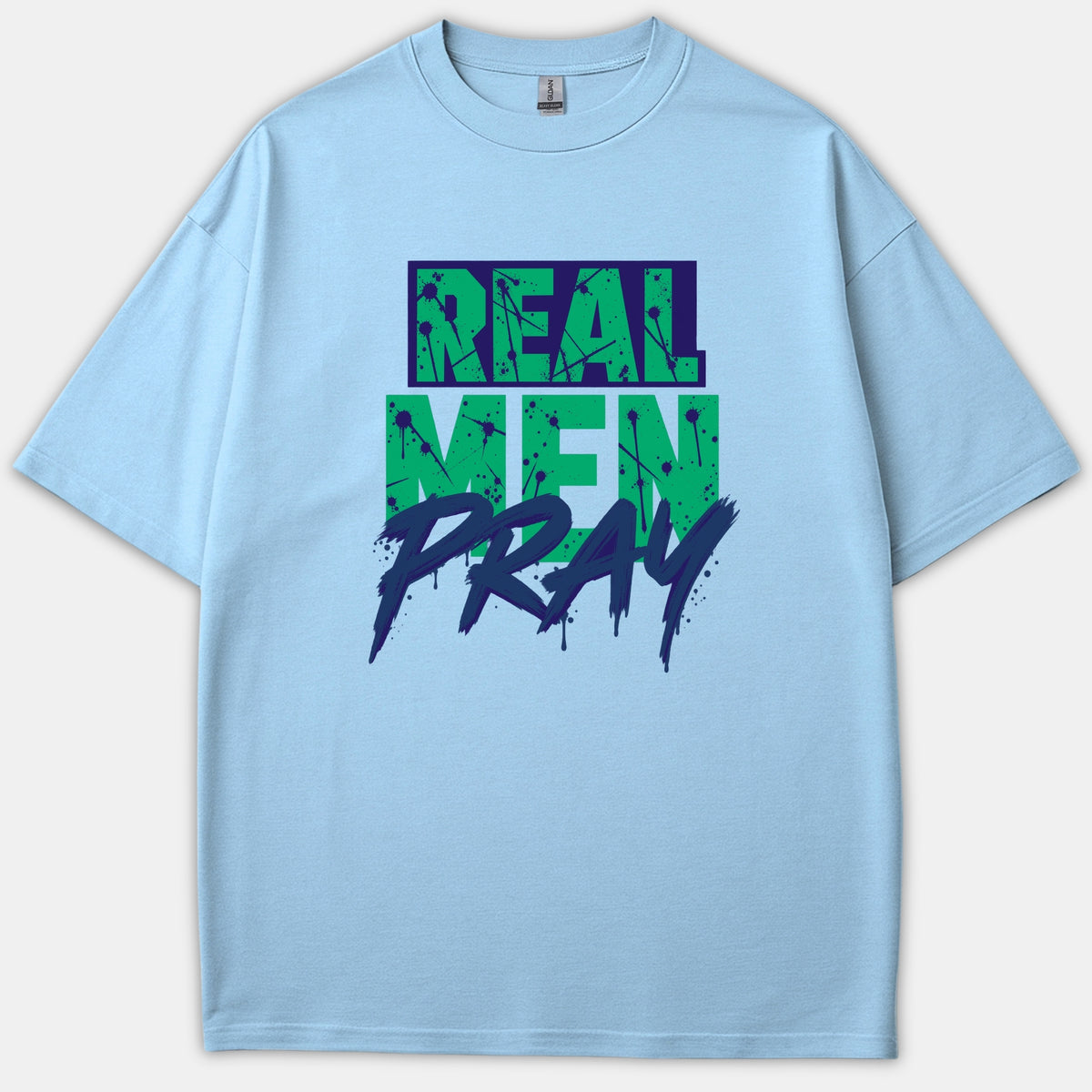 A light blue t-shirt featuring the phrase REAL MEN PRAY in a bold green and navy graphic paint-splatter typography.