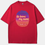 A red Christian t-shirt featuring a colorful gradient fingerprint graphic with the text 'He knows my name ISAIAH 43:1' printed across the chest.