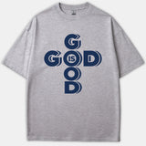 A gray t-shirt featuring a dark navy graphic print reading God Is Good styled in a cross configuration.