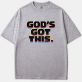 A gray graphic t-shirt featuring the bold phrase 'GOD'S GOT THIS.' in black lettering with colorful yellow, red, and blue layered drop shadow effects.