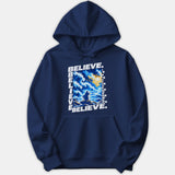 A navy blue hoodie featuring a graphic print framed with the word BELIEVE, depicting a robed figure standing before parting stormy sea waves under a bright yellow sky.