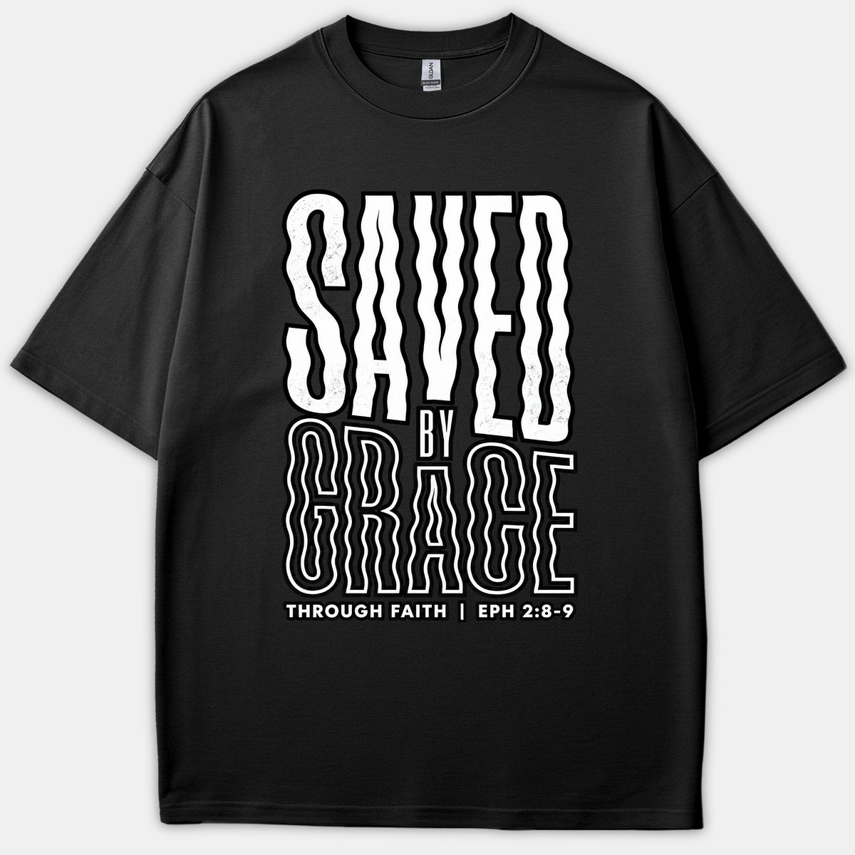 A black t-shirt featuring a wavy, retro-style graphic text that reads SAVED BY GRACE THROUGH FAITH with the scripture reference EPH 2:8-9.