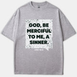 A gray t-shirt featuring a distressed white graphic that reads 'GOD, BE MERCIFUL TO ME, A SINNER' alongside the Scripture reference 'LUKE 18:13'.
