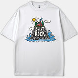 A white Christian t-shirt featuring a colorful graphic illustration of a house on a rock surrounded by ocean waves with the text Built On The Rock Matt. 7:24.