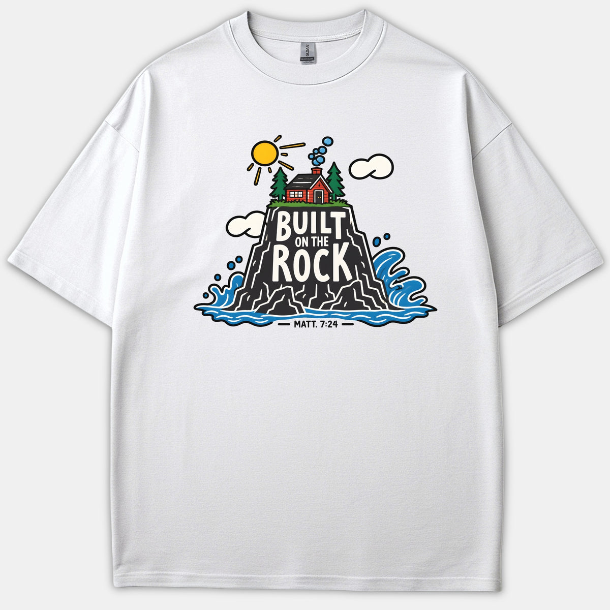 A white Christian t-shirt featuring a colorful graphic illustration of a house on a rock surrounded by ocean waves with the text Built On The Rock Matt. 7:24.