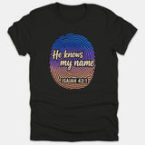 A black t-shirt featuring a colorful gradient fingerprint graphic with the phrase 'He knows my name' and the Scripture reference 'ISAIAH 43:1'.