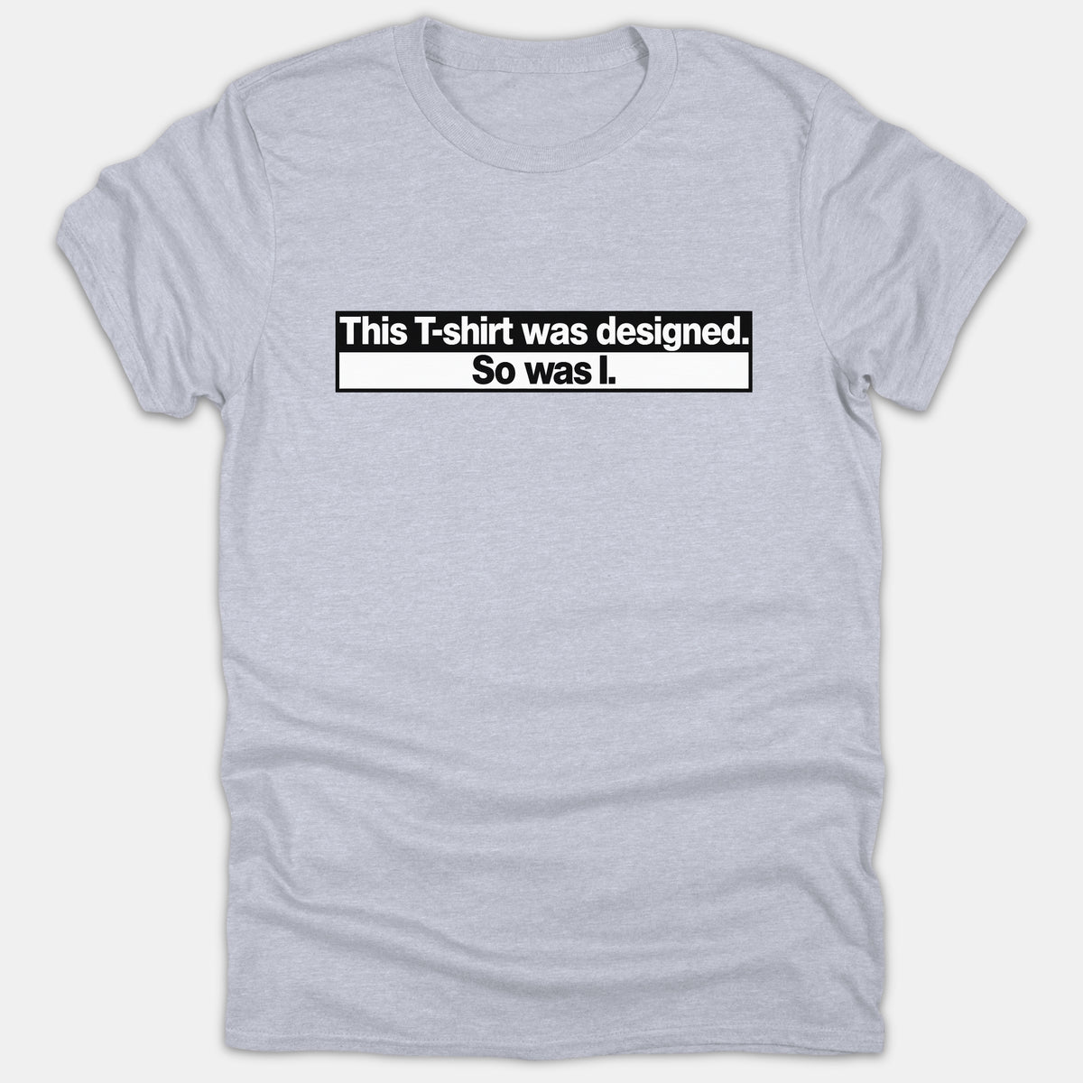 A light gray t-shirt featuring a bold black and white box graphic with text reading 'This T-shirt was designed. So was I.'