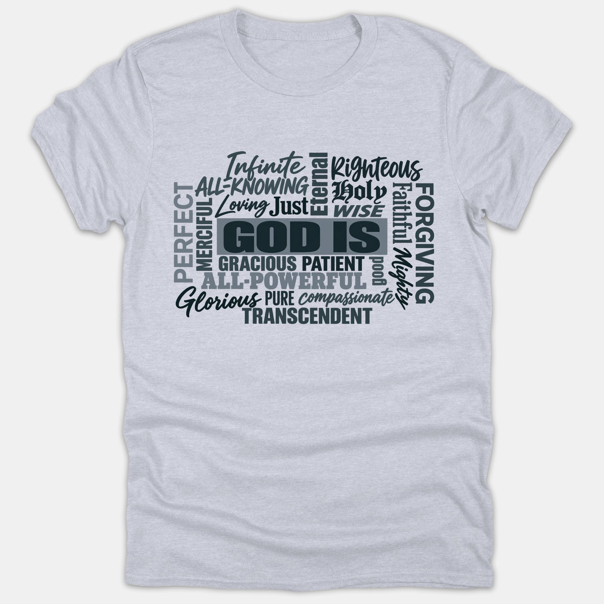 A gray Christian t-shirt featuring a word cloud design centered on 'GOD IS' surrounded by various divine attributes in dark typography.