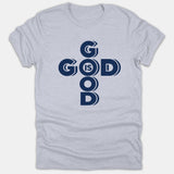 A light gray t-shirt featuring a dark navy blue graphic arranged in a cross layout reading God Is Good.