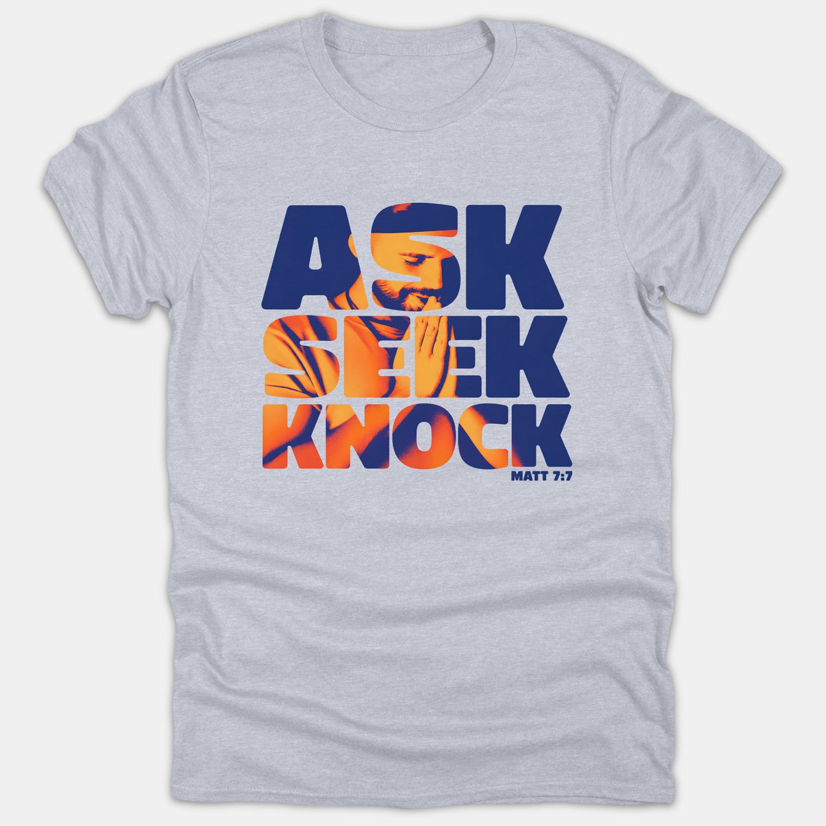 A gray t-shirt featuring a bold blue and orange graphic that reads 'ASK SEEK KNOCK MATT 7:7' with an image of a praying person inside the lettering.