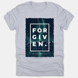 A light gray Christian t-shirt displaying a starry night graphic with northern lights over mountains, bold white text reading FORGIVEN, and the reference Colossians 2:13.