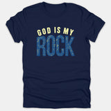 A navy blue t-shirt featuring the Christian phrase 'GOD IS MY ROCK' printed across the chest in pale yellow and distressed blue typography.