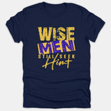 A navy blue t-shirt featuring the Christian message 'Wise Men Still Seek Him' in a bold yellow and purple distressed typography style.