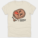 A beige Christian T-shirt featuring a cartoon tombstone graphic with crossed-out eyes and the scripture quote from 1 Corinthians 15:26.