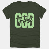 A dark green Christian t-shirt featuring 'GOD' in bold light green block letters overlaid with 'First' in black script and 'MATTHEW 6:33' below.