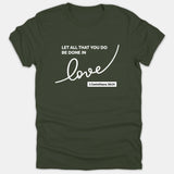 A dark green Christian t-shirt featuring the white text 'Let all that you do be done in love' alongside the verse reference 1 Corinthians 16:14.